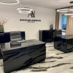 Wnętrze nowoczesnej kancelarii adwokackiej z czarnymi, lakierowanymi meblami, okrągłymi lampami i marmurową podłogą. Na ścianie logo i napis 'Kancelaria Adwokacka Anna Nowak'.