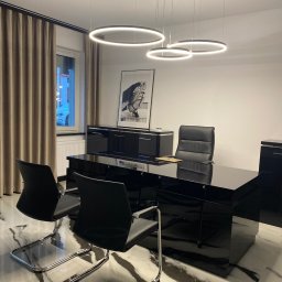 Kancelaria Adwokacka Anna Nowak - Nowoczesne biuro adwokackie z czarnym lakierowanym biurkiem, skórzanymi krzesłami i marmurową podłogą. Okrągłe lampy wiszące dodają elegancji.