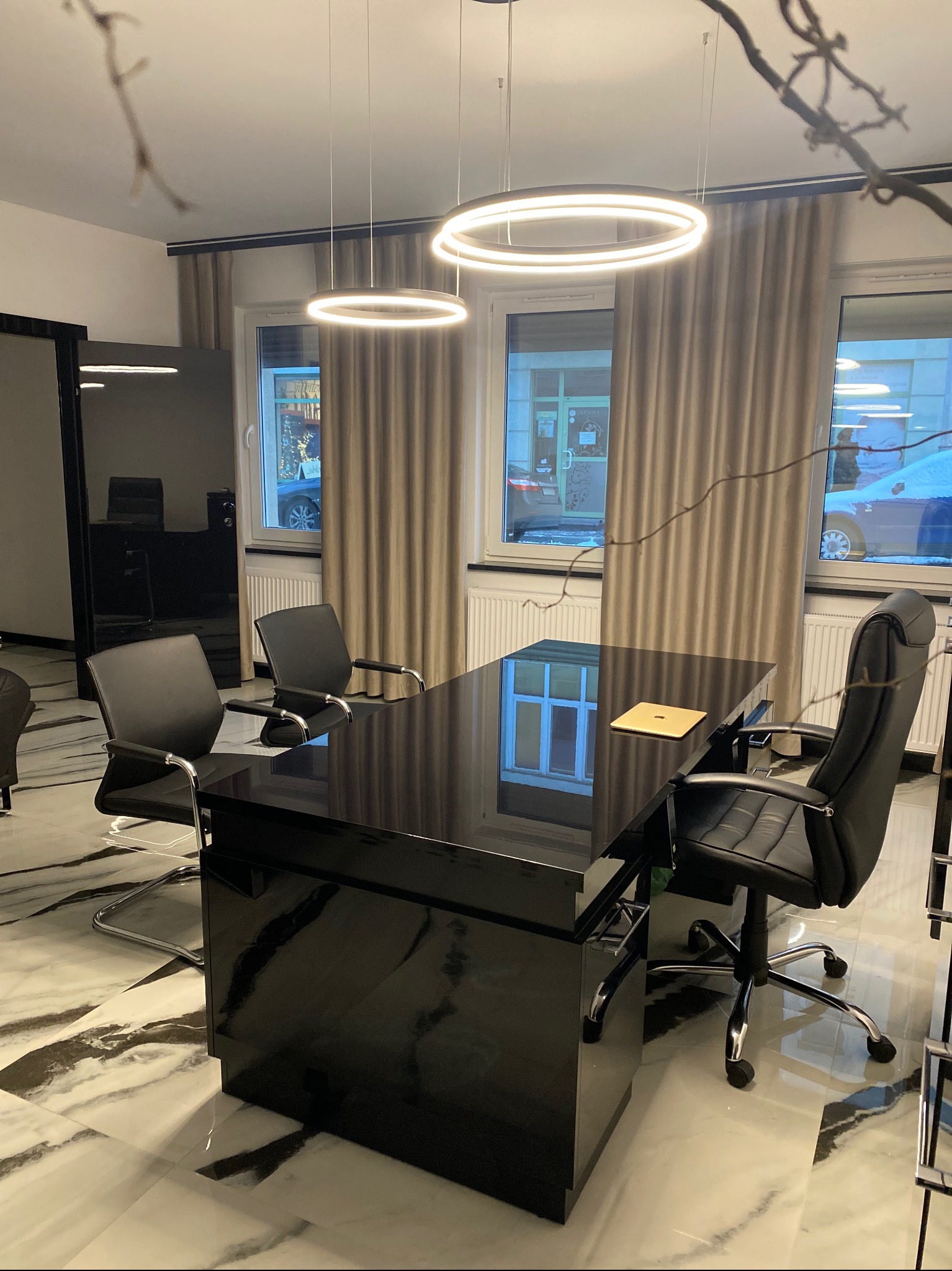 Eleganckie biuro: czarne biurko z laptopem, krzesła, marmurowa podłoga i okrągłe lampy sufitowe w jasnym wnętrzu z zasłonami.