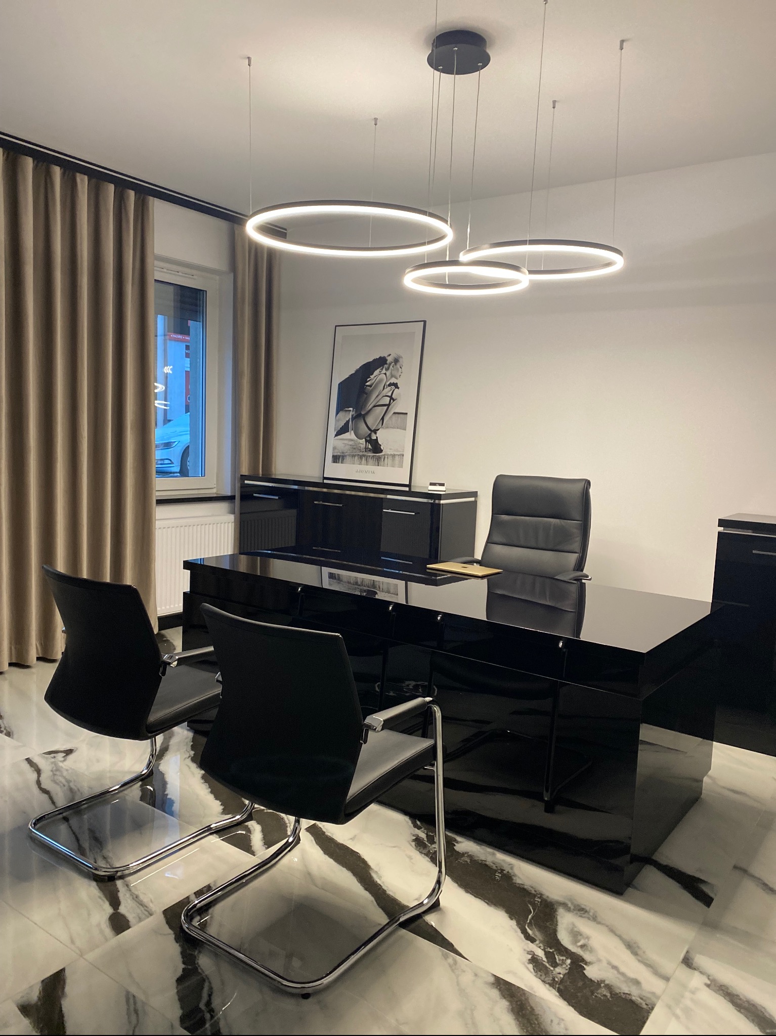 Nowoczesne biuro adwokackie z czarnym lakierowanym biurkiem, skórzanymi krzesłami i marmurową podłogą. Okrągłe lampy wiszące dodają elegancji.