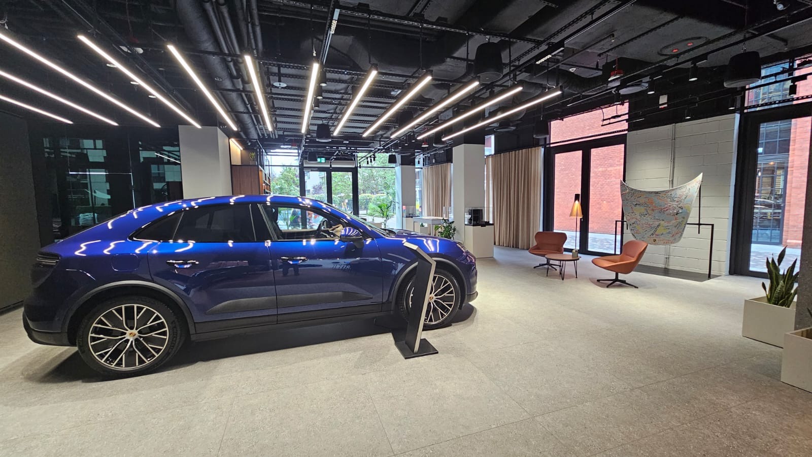 Nowoczesne wnętrze biura z ciemnym sufitem i liniowym oświetleniem LED, na podłodze szary gres, w tle krzesła i instalacja artystyczna, na pierwszym planie niebieski samochód.