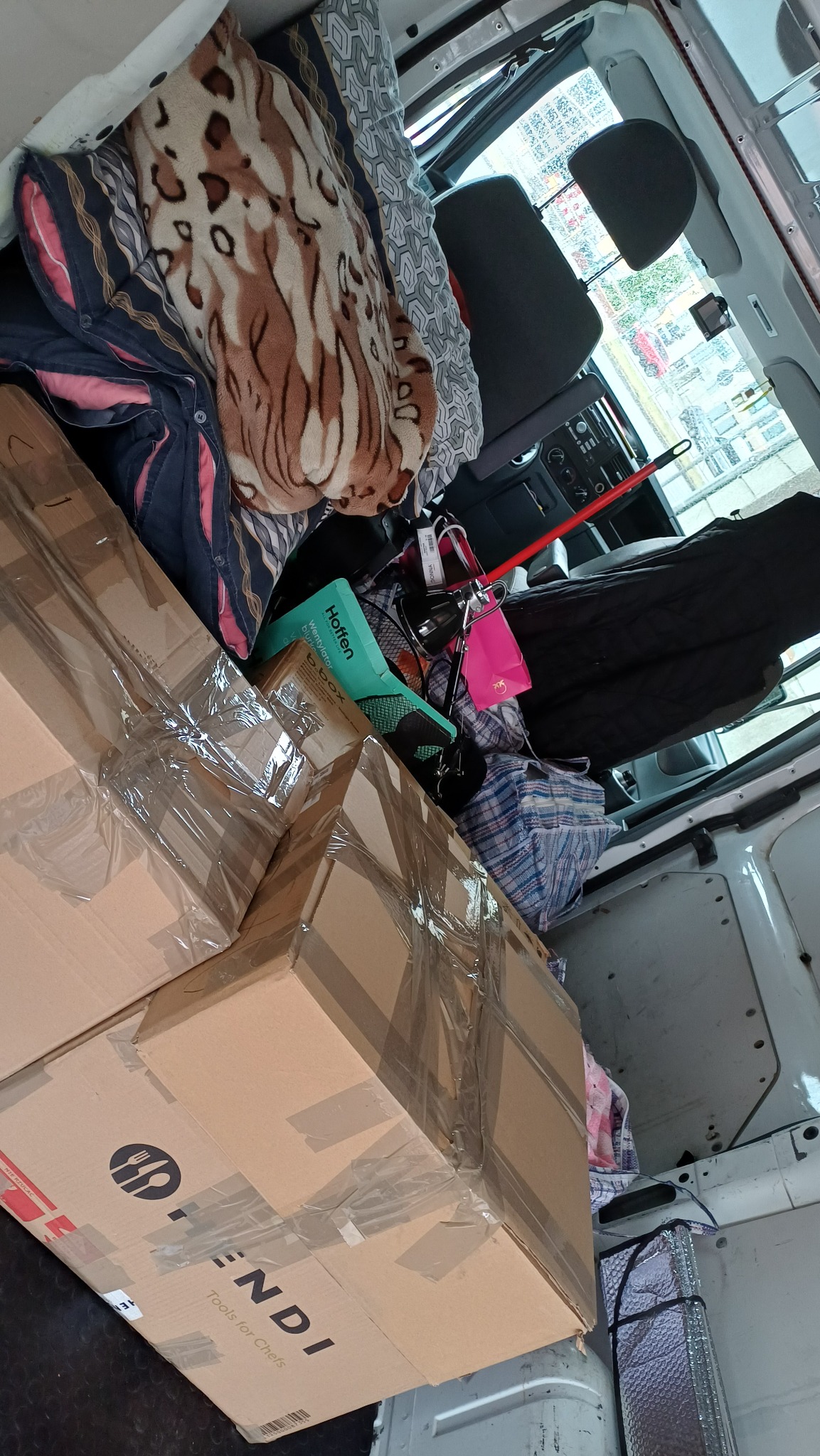 Wnętrze busa wypełnione kartonami, torbami i kocami podczas przeprowadzki. Widoczne zabezpieczone paczki i osobiste przedmioty gotowe do transportu.