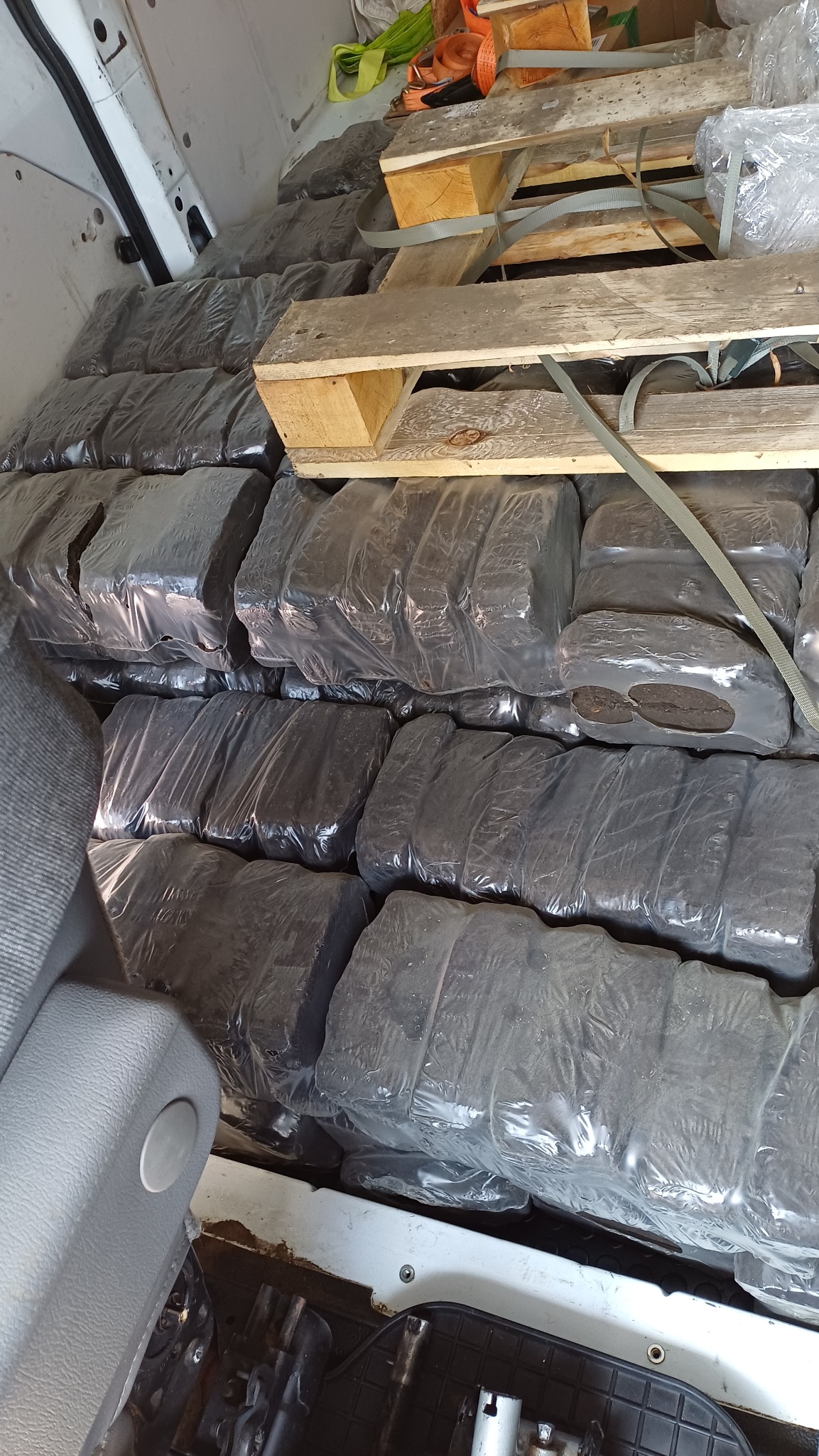 Wnętrze busa wypełnione paletami i towarem zabezpieczonym folią, gotowym do transportu. Widoczne elementy mocujące ładunek i fragment fotela kierowcy.