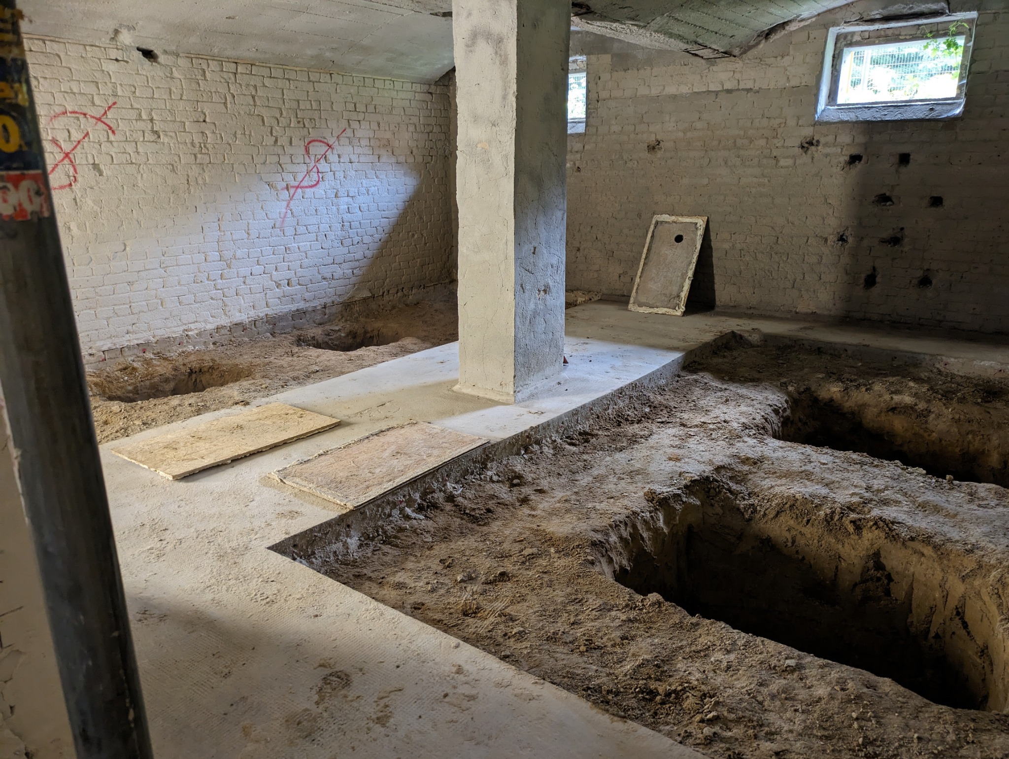 Piwnica w trakcie prac ziemnych: wykopane rowy w podłodze, odsłonięta cegła, podpory. Prace przygotowawcze do dalszych etapów budowlanych.