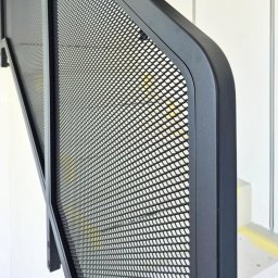 CROMO JMI Rozalia Milbrod - Czarna, metalowa balustrada schodowa z siatką o drobnych oczkach, zamontowana na białej ścianie. Widoczny fragment schodów z żółtą taśmą.