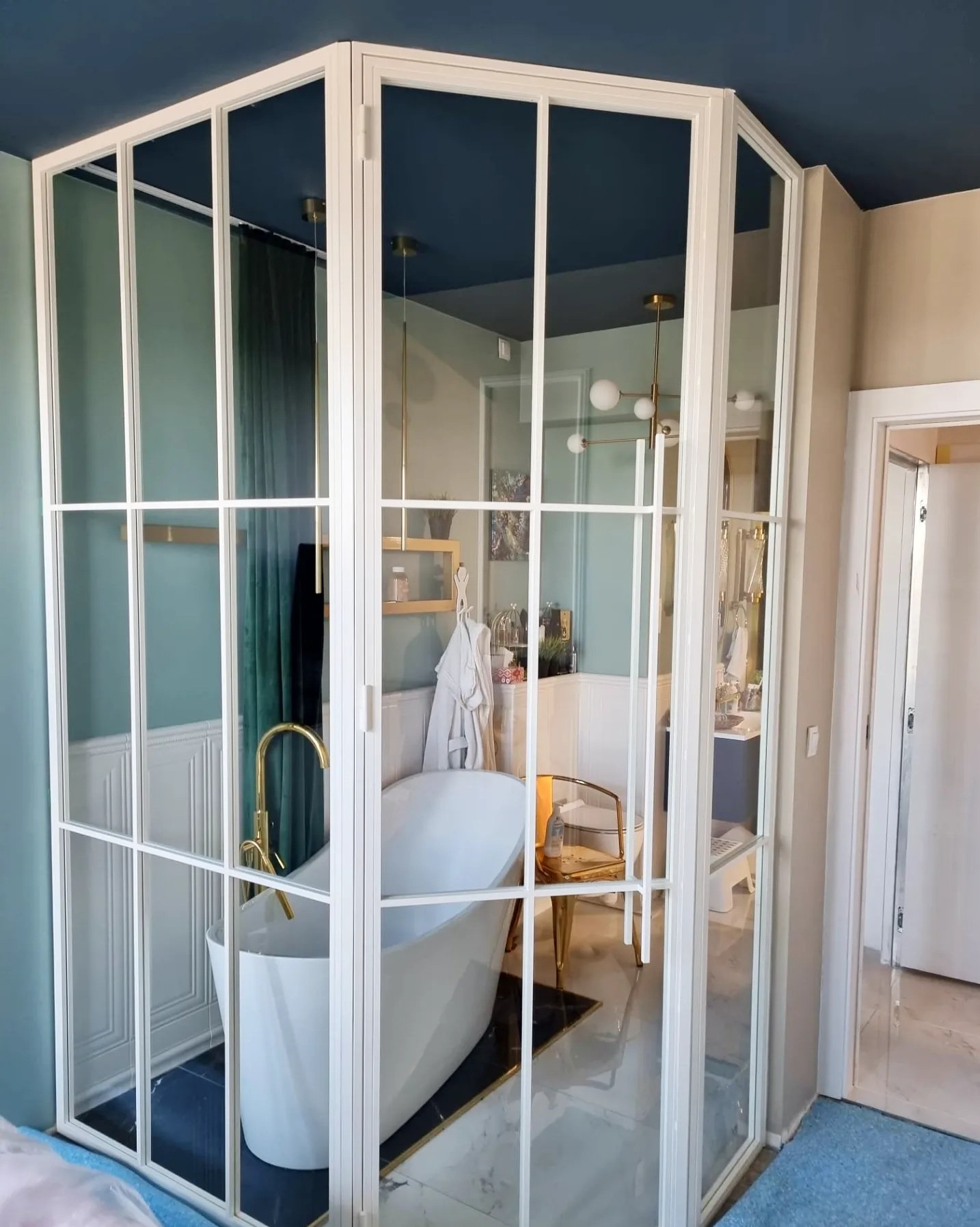 Nowoczesna kabina prysznicowa ze szklanymi ściankami i białymi profilami, widoczna wanna wolnostojąca i elementy wystroju łazienki w stylu glamour.