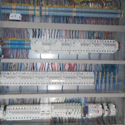 Rozdzielnia elektryczna z licznymi przewodami i zabezpieczeniami, widok od frontu, ukazujący skomplikowaną sieć połączeń i precyzyjny montaż elementów.