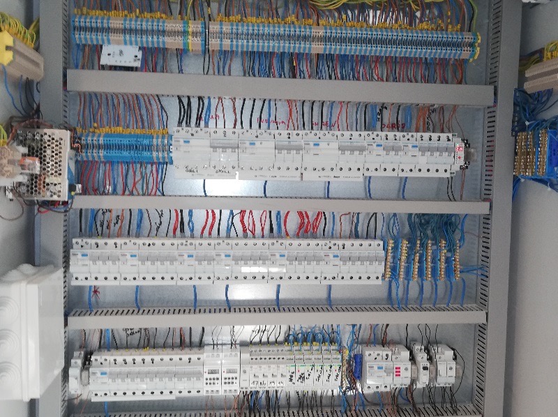 Rozdzielnia elektryczna z licznymi przewodami i zabezpieczeniami, widok od frontu, ukazujący skomplikowaną sieć połączeń i precyzyjny montaż elementów.