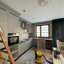 NEG DESIGN NATALIA GRZYWACZ - Montaż kuchni w trakcie realizacji w Warszawie. Widoczny odkurzacz, drabina i narzędzia. Elementy wykończeniowe sufitu dodają elegancji.