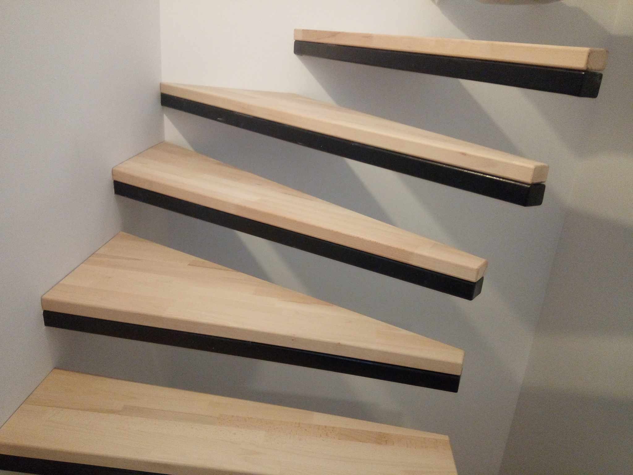 Nowoczesne schody wiszące z jasnego drewna i czarnymi elementami mocującymi, osadzone w minimalistycznym, białym wnętrzu.