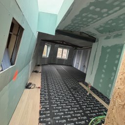 Kamil Tylus - Poddasze w trakcie wykańczania: płyty karton-gips na ścianach i suficie, podkład pod panele podłogowe z widocznymi napisami, okna dachowe.