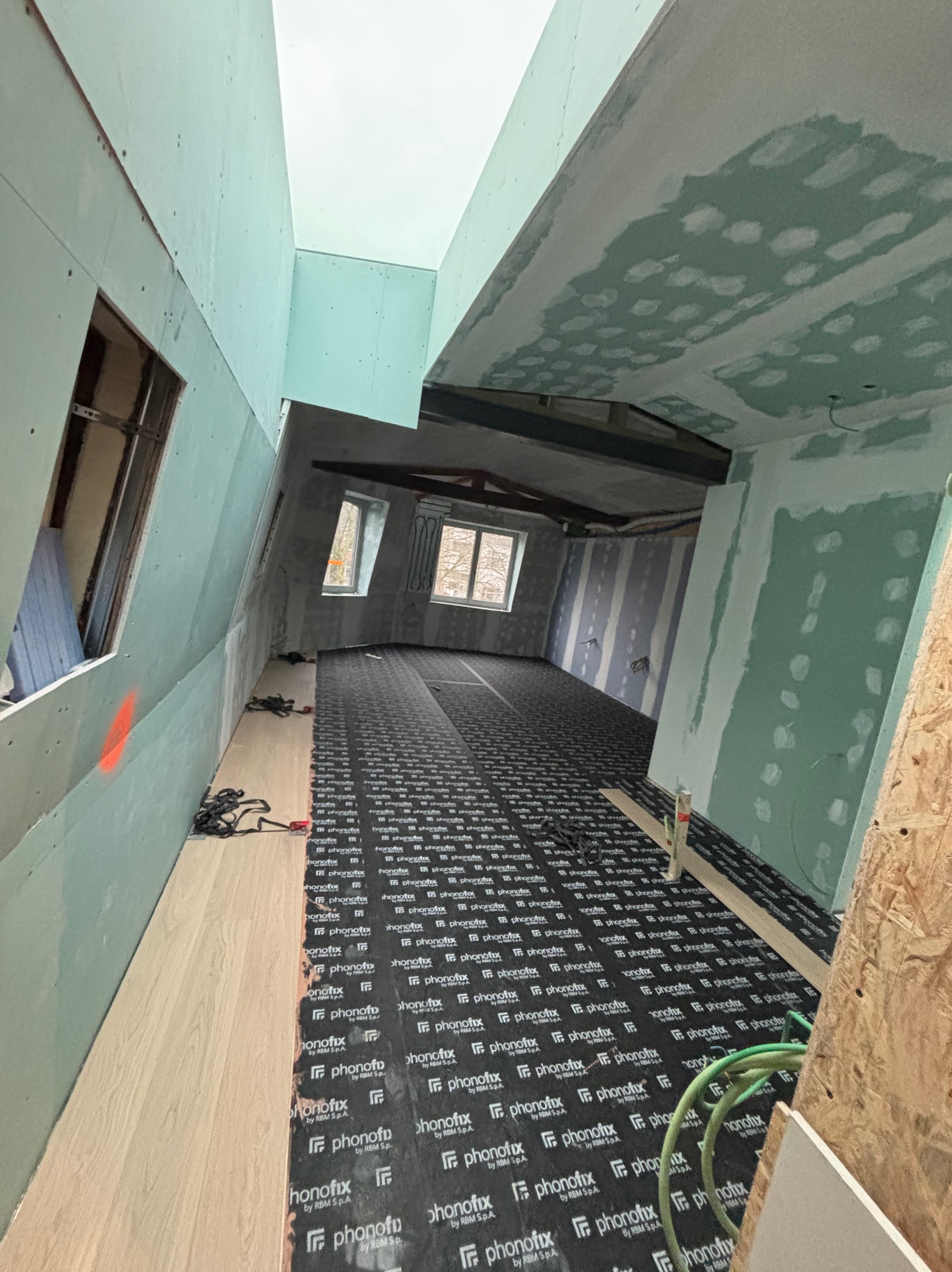 Poddasze w trakcie wykańczania: płyty karton-gips na ścianach i suficie, podkład pod panele podłogowe z widocznymi napisami, okna dachowe.