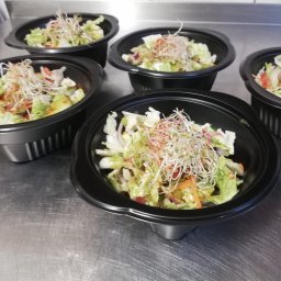 AKK SPÓŁKA Z OGRANICZONĄ ODPOWIEDZIALNOŚCIĄ - Sałatki z warzywami i kiełkami w czarnych miseczkach na metalowym blacie, gotowe do cateringu. Widok z góry.