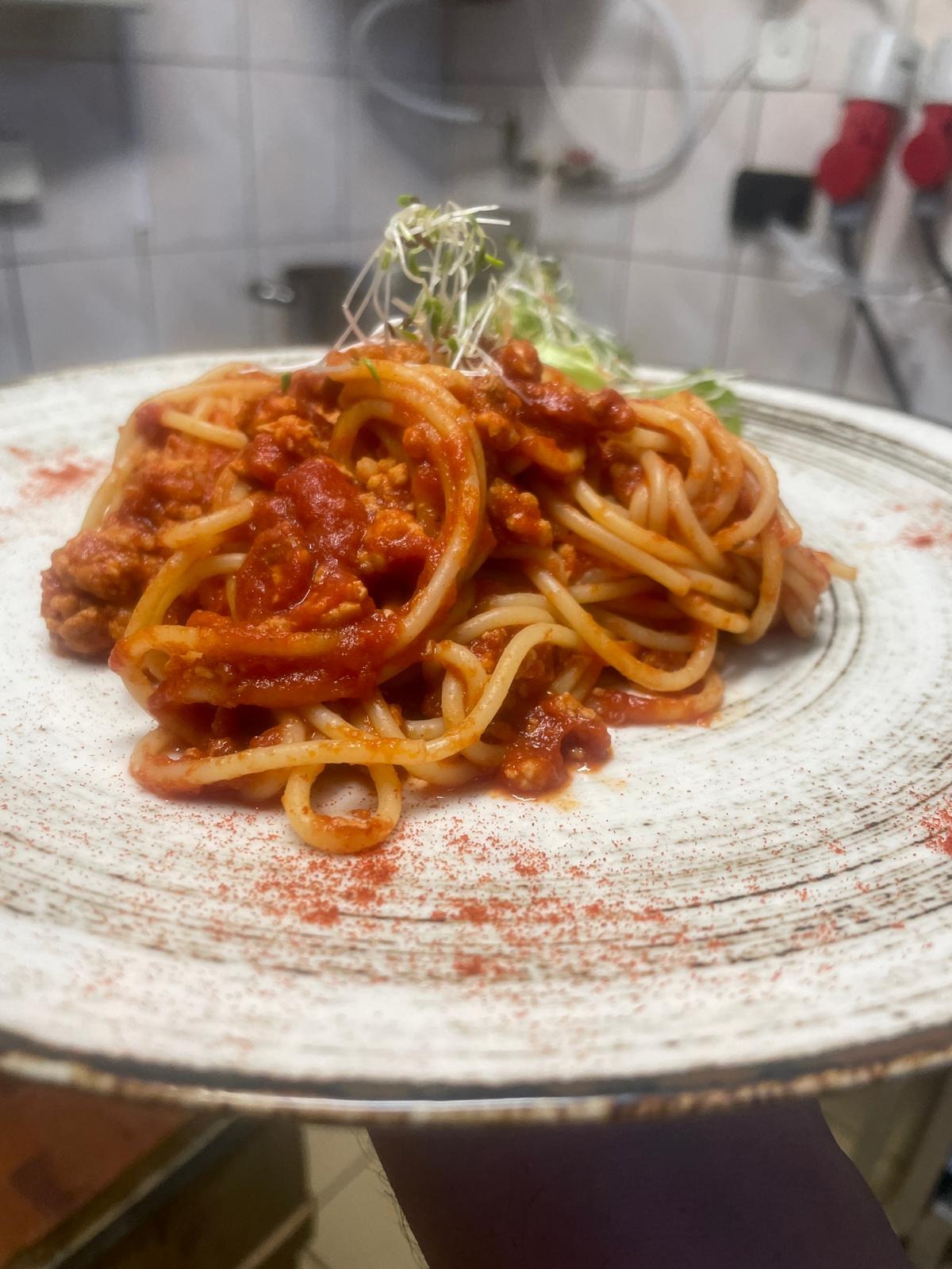 Apetyczne spaghetti bolognese na talerzu z rustykalnym wzorem, ozdobione świeżymi kiełkami i delikatnie posypane papryką, gotowe do podania na imprezie.