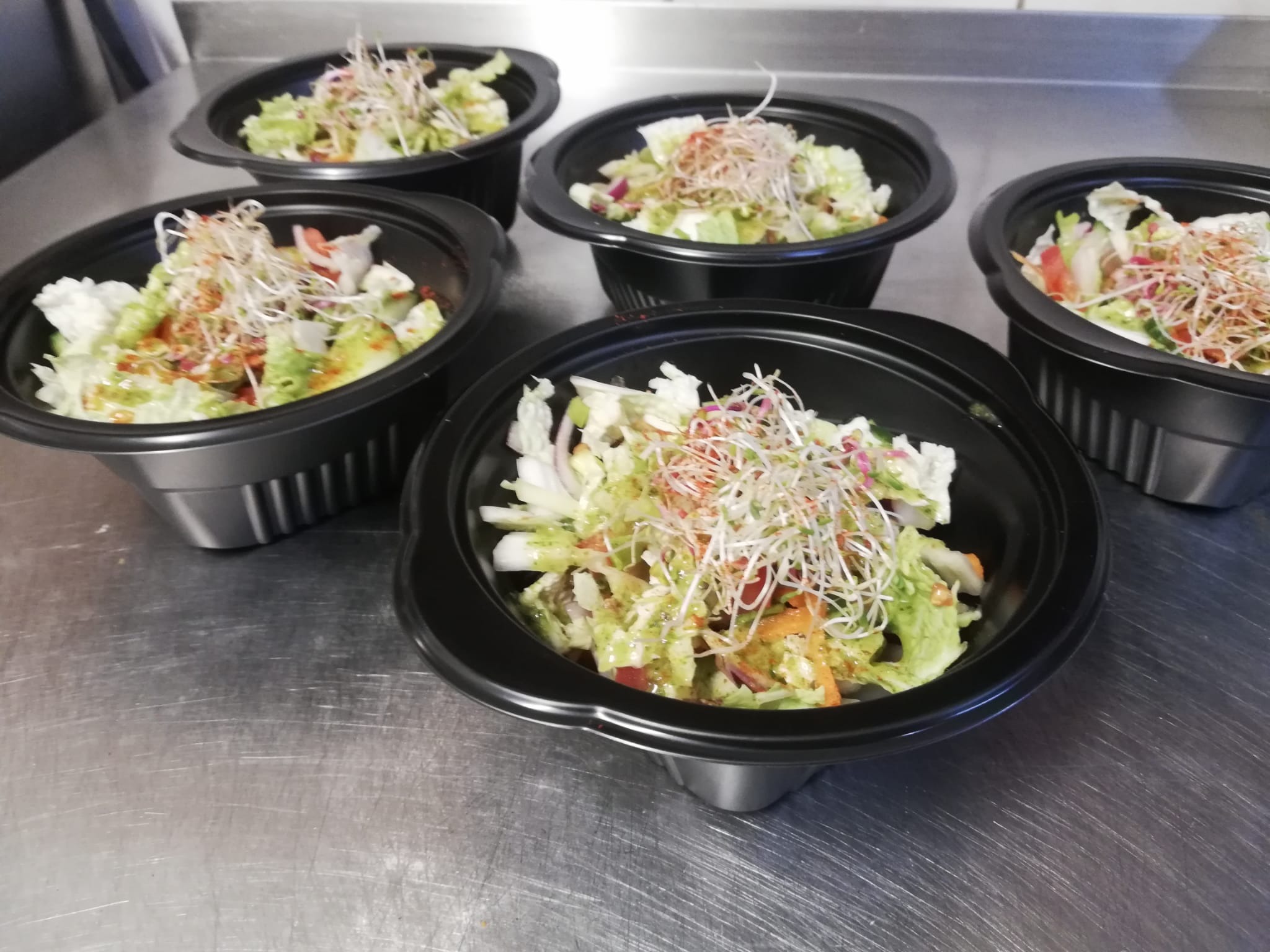 Sałatki z warzywami i kiełkami w czarnych miseczkach na metalowym blacie, gotowe do cateringu. Widok z góry.