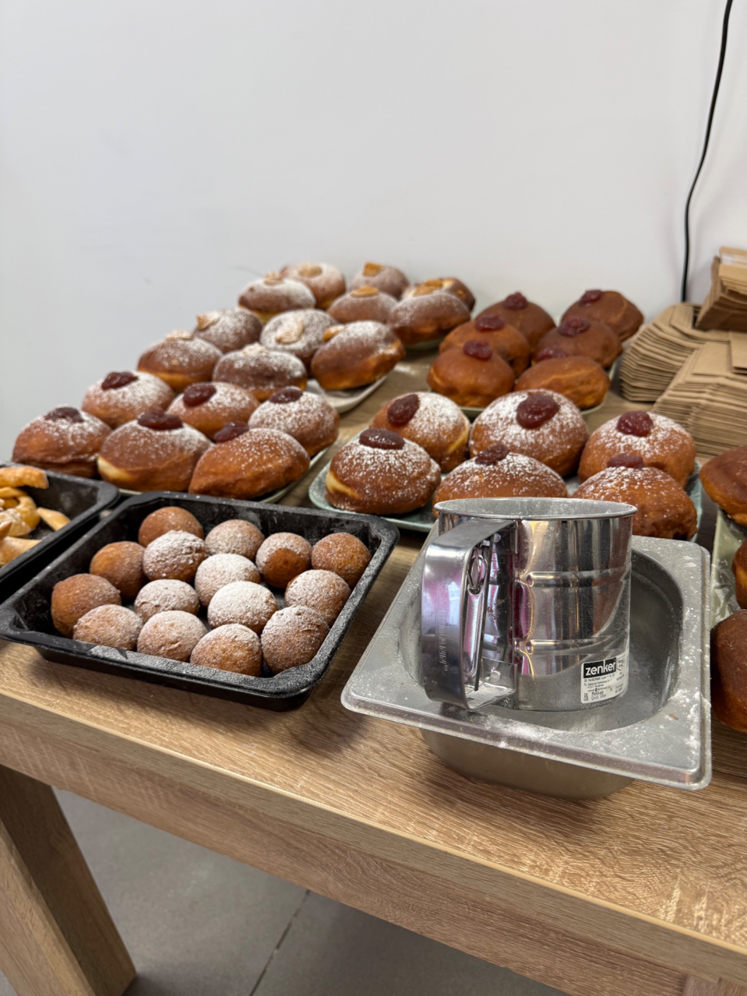 Słodki stół z pączkami z marmoladą i posypką z cukru pudru, obok metalowe sitko do cukru pudru, gotowe do serwowania na imprezie.
