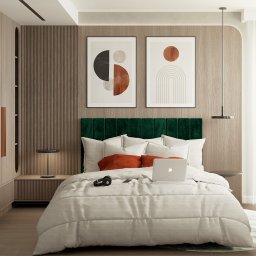 Twoje Nowe Studio Projektowe Ewa Kromska - Jasna sypialnia z łóżkiem, zielonym zagłówkiem i drewnianą zabudową. Na łóżku laptop i słuchawki. Dwa abstrakcyjne obrazy nad łóżkiem. Minimalistyczny design.