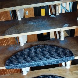 Michał Stolarczyk - Drewniane schody z półokrągłymi, szarymi nakładkami dywanowymi. Widok z góry, oświetlenie naturalne, wnętrze wykończone drewnem.