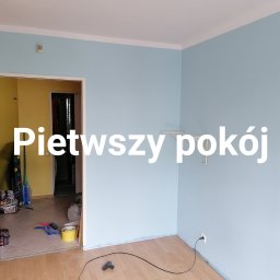Michał Stolarczyk - Błękitne ściany świeżo pomalowanego pokoju z drewnianą podłogą. Widoczne akcesoria malarskie w sąsiednim pokoju. Minimalistyczne wnętrze po odnowieniu.