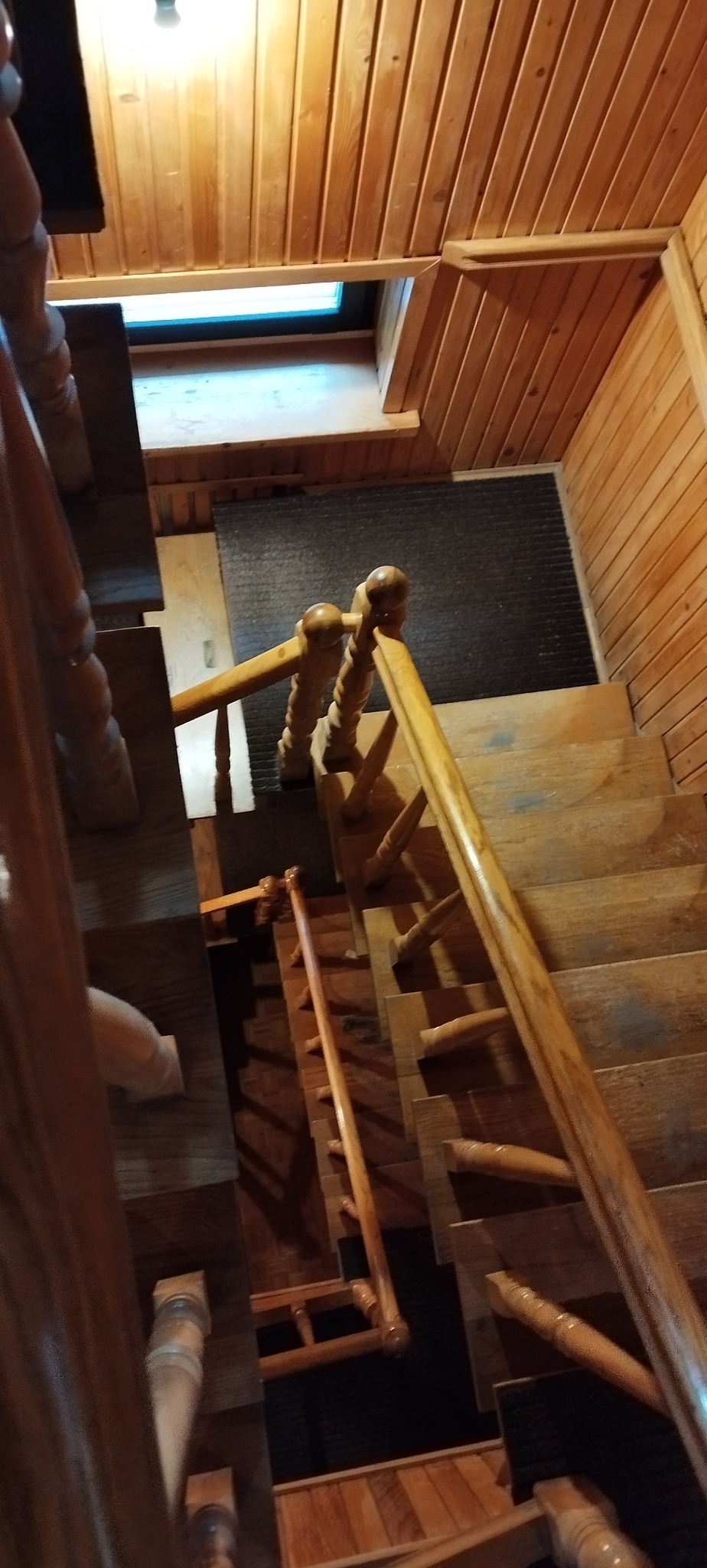 Drewniane schody z balustradą w domu z boazerią, widok z góry, oświetlone światłem z okna dachowego. Ciepłe odcienie drewna i klasyczny design.