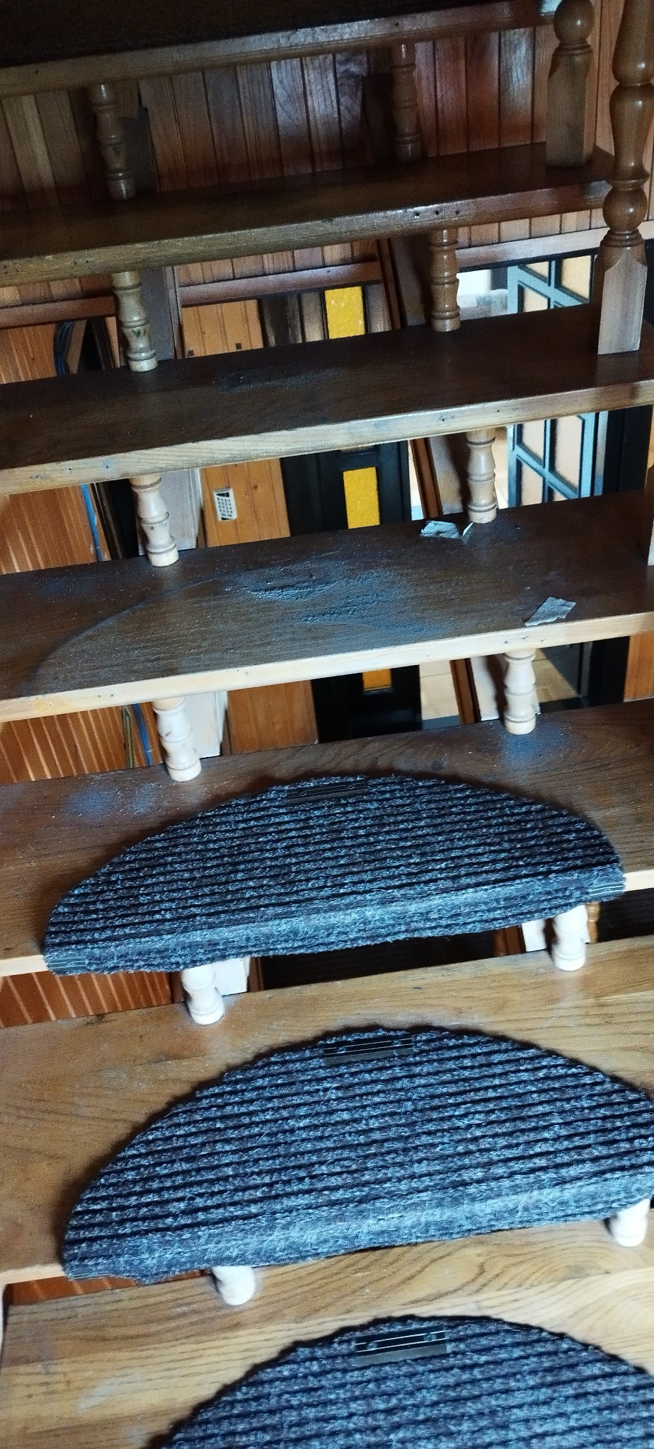 Drewniane schody z półokrągłymi, szarymi nakładkami dywanowymi. Widok z góry, oświetlenie naturalne, wnętrze wykończone drewnem.