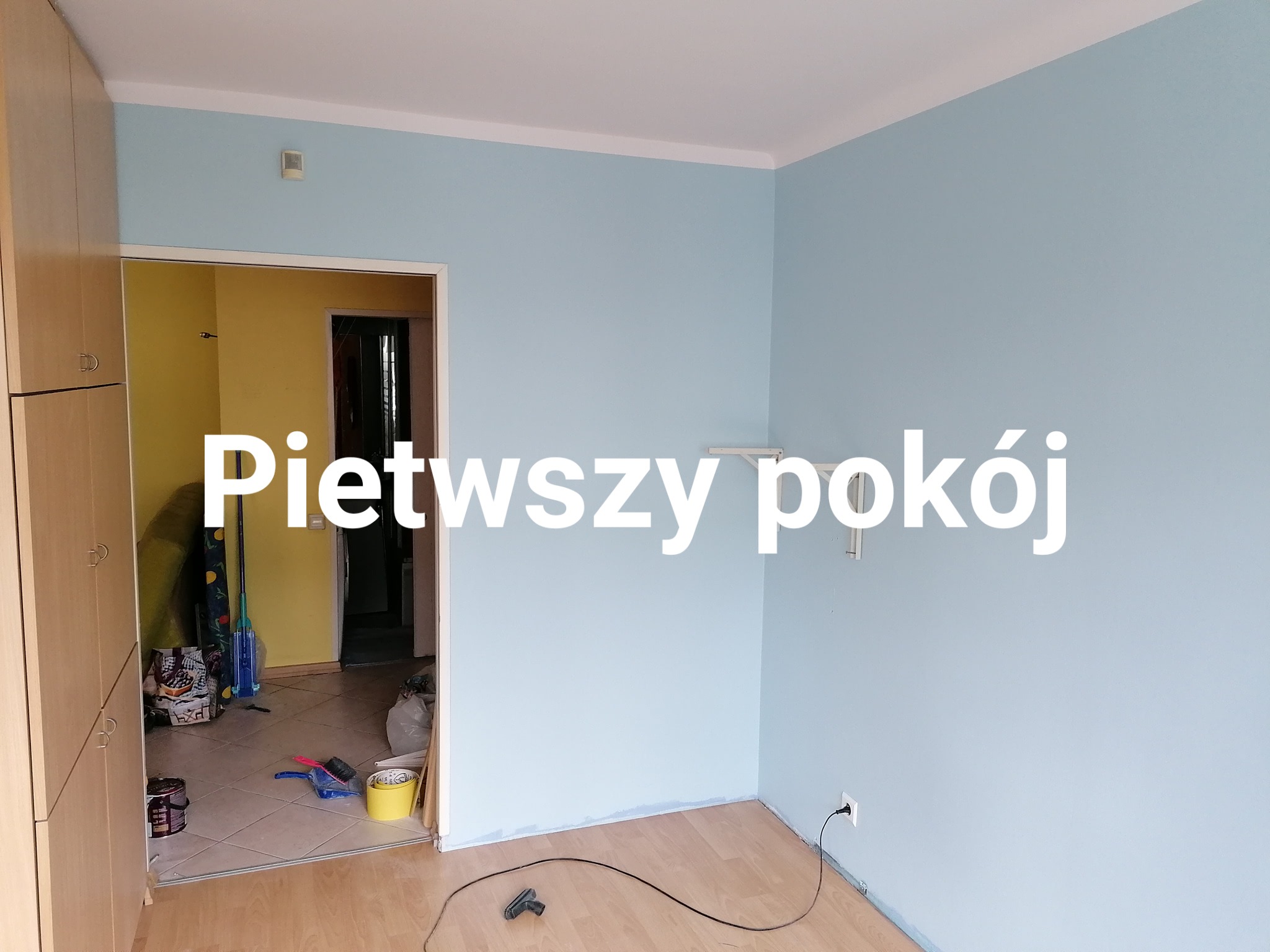 Błękitne ściany świeżo pomalowanego pokoju z drewnianą podłogą. Widoczne akcesoria malarskie w sąsiednim pokoju. Minimalistyczne wnętrze po odnowieniu.
