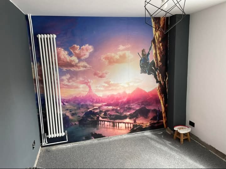 Pokój z fototapetą przedstawiającą krajobraz fantasy i wspinającą się postać. Biały grzejnik na szarej ścianie. Geometryczna lampa sufitowa i mały stołek w rogu.