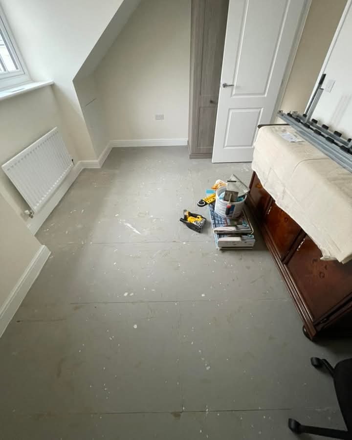 Przygotowanie podłoża pod panele w pokoju na poddaszu. Widoczne narzędzia, farba i płyty wyrównujące. Ściany pomalowane na jasny kolor, okno dachowe.