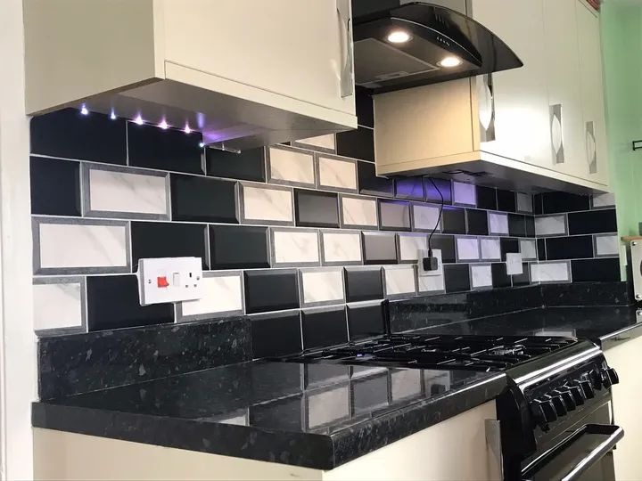 Wykończona kuchnia z czarno-białą mozaiką z płytek i czarnym blatem. Widoczny fragment kuchenki gazowej i oświetlenie podszafkowe LED.