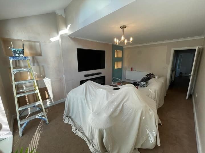 Pokój w trakcie prac wykończeniowych: ściany po szpachlowaniu, drabina malarska, meble zabezpieczone folią, widoczny fragment sufitu z oświetleniem.