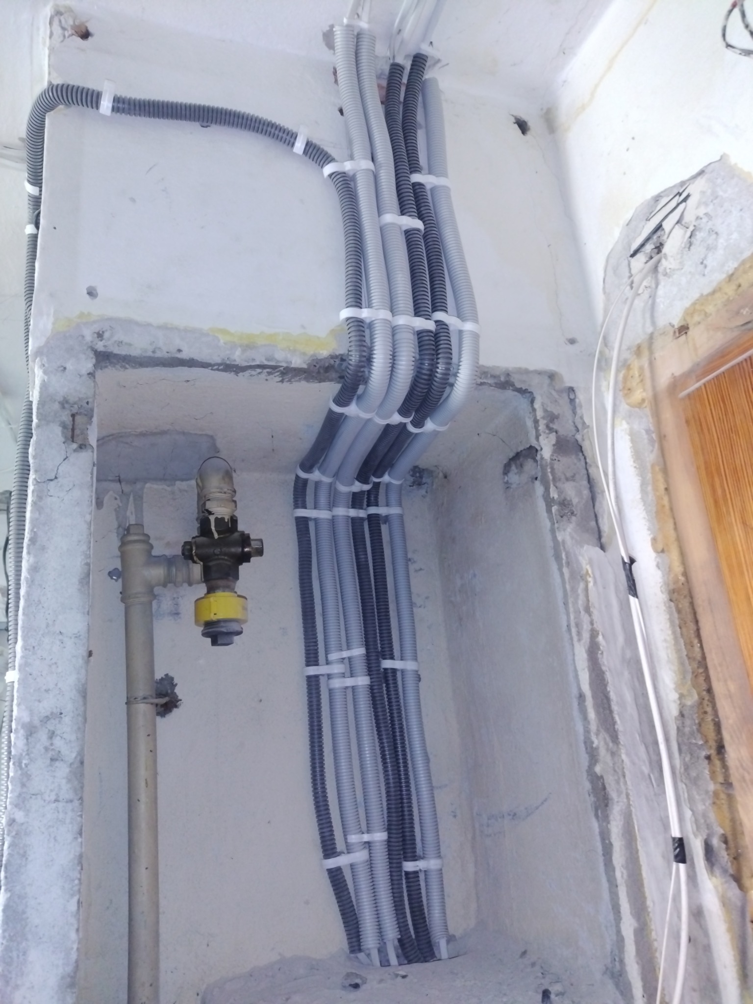 Szare i czarne rury karbowane, zabezpieczone białymi opaskami, prowadzone wzdłuż ściany w trakcie prac remontowych. Widoczny fragment instalacji gazowej.