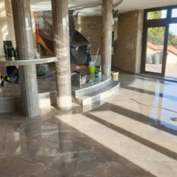 Wykończone wnętrze z połyskującą, marmurkową podłogą i kamiennymi ścianami. Widoczne kolumny i schody wykończone tym samym materiałem co podłoga. Częściowo zakryte elementy w folii.