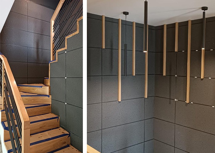 Nowoczesne wykończenie klatki schodowej z szarą okładziną ścienną, drewnianymi elementami dekoracyjnymi i minimalistycznym oświetleniem.