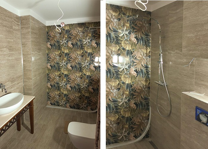Wykończona łazienka z kabiną prysznicową i umywalką. Na ścianach płytki imitujące trawertyn oraz wzorzyste płytki w strefie prysznica z motywem roślinnym.