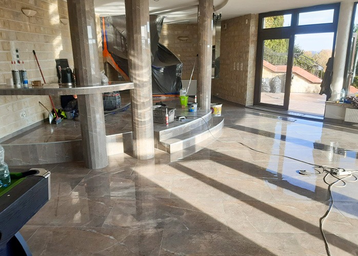 Wykończone wnętrze z połyskującą, marmurkową podłogą i kamiennymi ścianami. Widoczne kolumny i schody wykończone tym samym materiałem co podłoga. Częściowo zakryte elementy w folii.