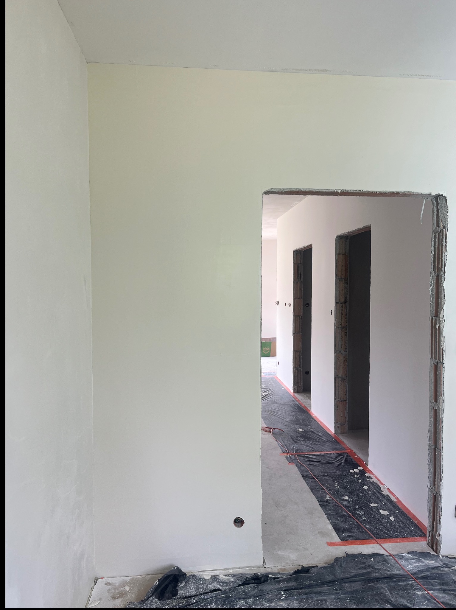 Wnętrze po szpachlowaniu: gładkie, białe ściany, przygotowane do malowania. Widoczne otwory drzwiowe i folia ochronna na podłodze. Minimalistyczny kadr, surowy stan wykończenia.