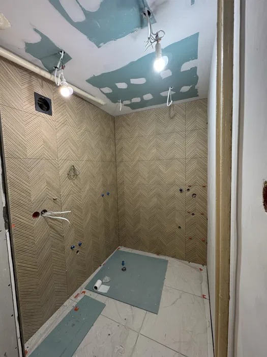 Wnętrze łazienki w trakcie prac wykończeniowych: ułożona glazura w jodełkę na ścianach, częściowo wykończony sufit z widocznymi instalacjami elektrycznymi.
