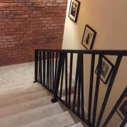 Nowoczesna, czarna balustrada metalowa na schodach z wykładziną, ściana z cegły i wiszące obrazy, oświetlenie górne.