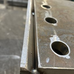 TopMetalWork - Spoina łącząca dwie metalowe płyty z otworami, widoczna z bliska. Szlifowana krawędź i ślady po obróbce. Detal konstrukcji stalowej w hali.