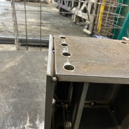 TopMetalWork - Metalowa konstrukcja spawana z otworami, widoczne spawy i elementy konstrukcyjne. W tle warsztat z elementami metalowymi.