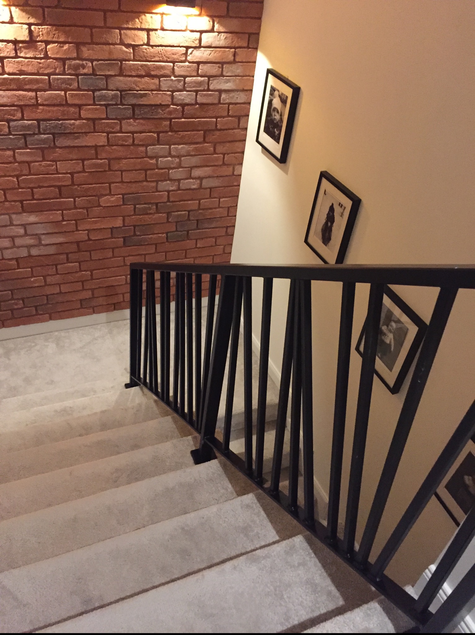 Nowoczesna, czarna balustrada metalowa na schodach z wykładziną, ściana z cegły i wiszące obrazy, oświetlenie górne.