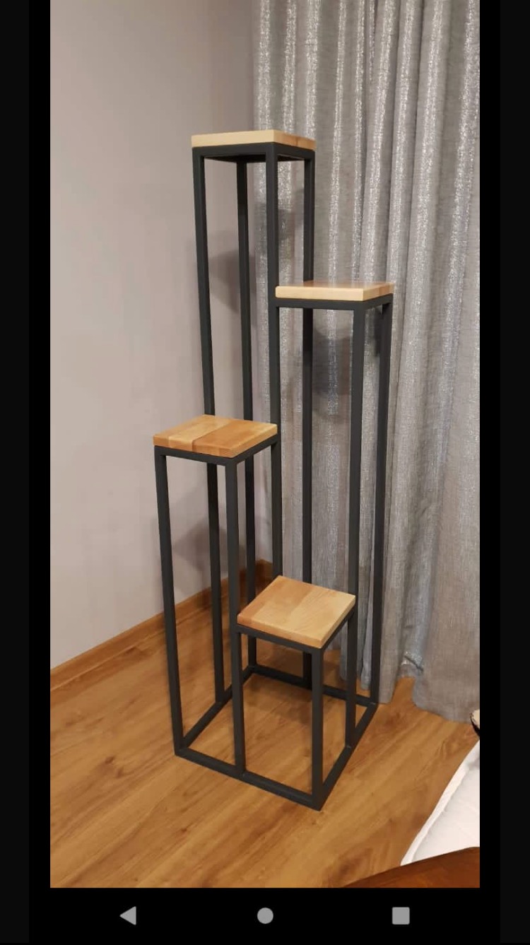 Komplet trzech kwietników metalowych z drewnianymi blatami, o różnych wysokościach, ustawionych na parkiecie, na tle ściany i zasłony.