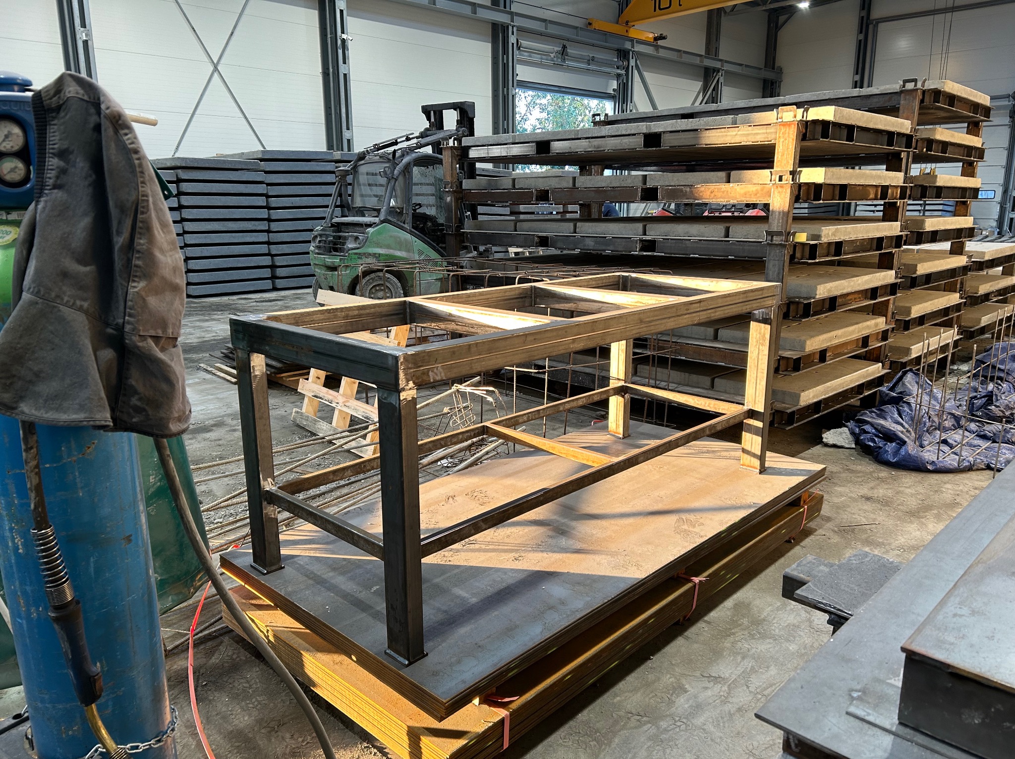 Konstrukcja metalowa stołu w warsztacie w Proszowicach. W tle wózek widłowy i stosy blach. Widoczny spawany szkielet stołu na palecie z blach.
