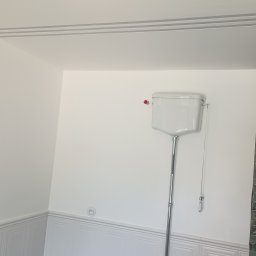 Stanisław szymulewski - Wykończona łazienka: białe ściany z dekoracyjnymi listwami, toaleta ze spłuczką na ścianie i zielona ściana z płytek z deszczownicą. Minimalistyczny design.