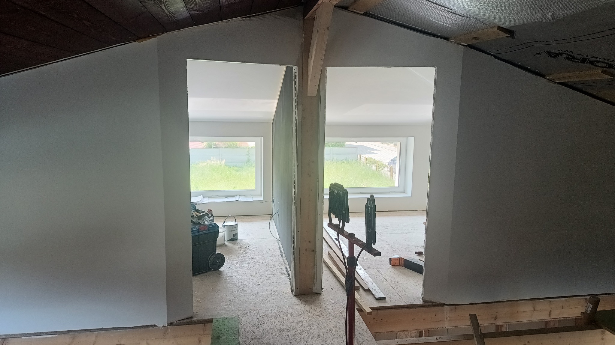 Montaż ścianki działowej z płyt gipsowo-kartonowych na poddaszu, widoczne narzędzia i materiały budowlane, okna w tle.