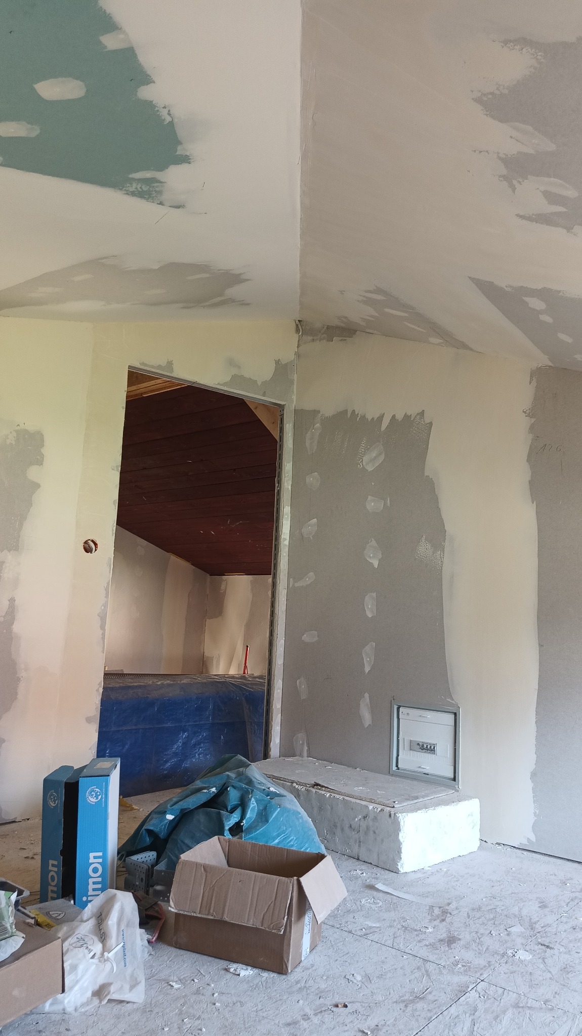 Wnętrze w trakcie prac wykończeniowych: ściany i sufit z widocznymi miejscami po szpachlowaniu, przygotowane do dalszych prac malarskich. Widoczne materiały budowlane.