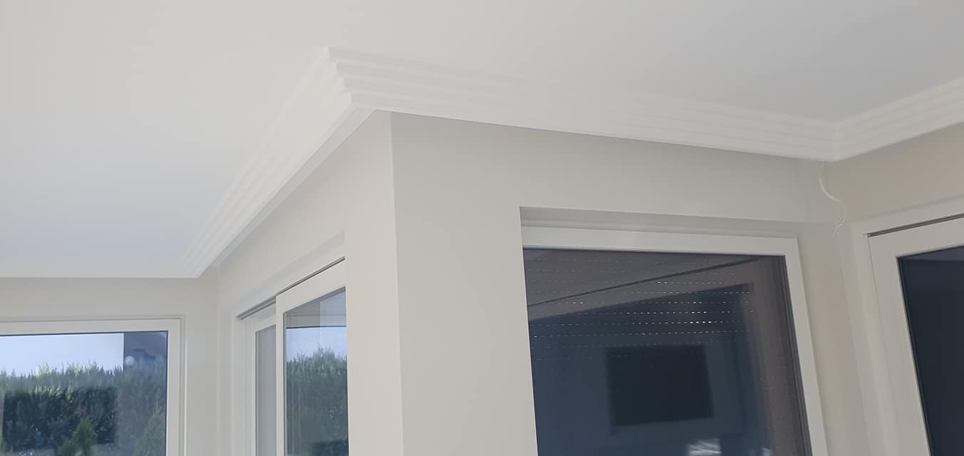 Jasne wnętrze po wykończeniu: białe ściany, okna z roletami i dekoracyjny gzyms sufitowy. Minimalistyczny design i dbałość o detale.