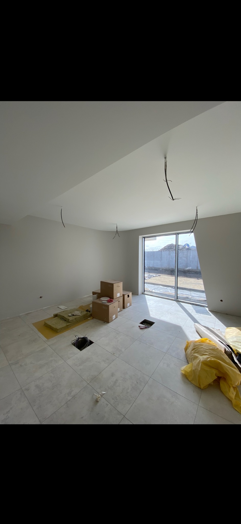 Wnętrze w trakcie prac w Wręczycy Małej: położona podłoga z płytek, przygotowane otwory w podłodze, instalacja elektryczna w suficie, okno z widokiem na zewnątrz.