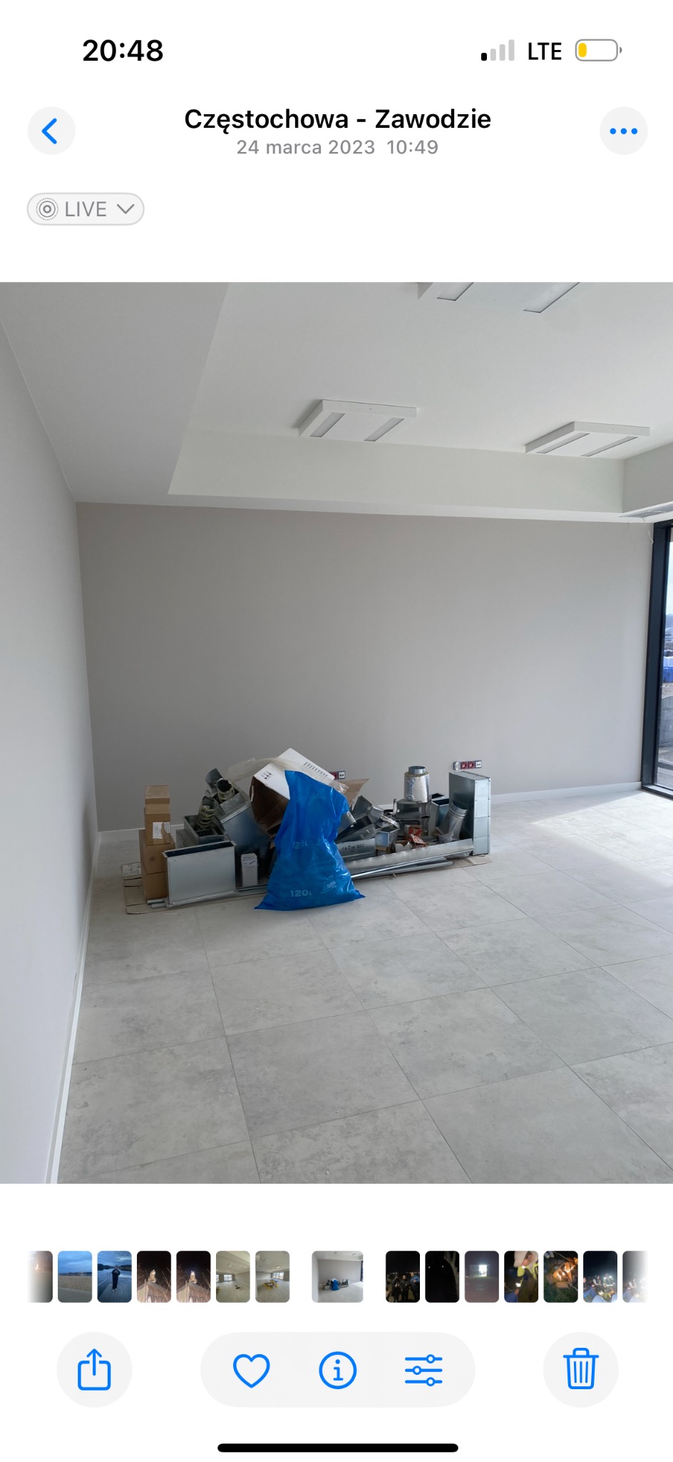 Wnętrze w trakcie remontu, z widocznym nagromadzeniem materiałów budowlanych i workiem na odpady na tle świeżo pomalowanej ściany i jasnych płytek podłogowych.