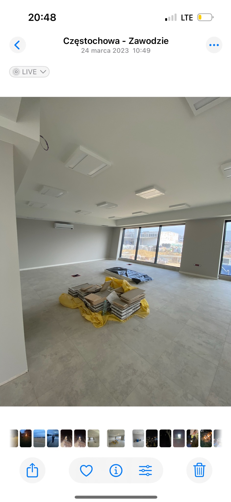 Jasne biuro w trakcie prac wykończeniowych: ułożona szara podłoga z płytek, okna, materiały budowlane na podłodze. Widoczny klimatyzator i oświetlenie sufitowe.